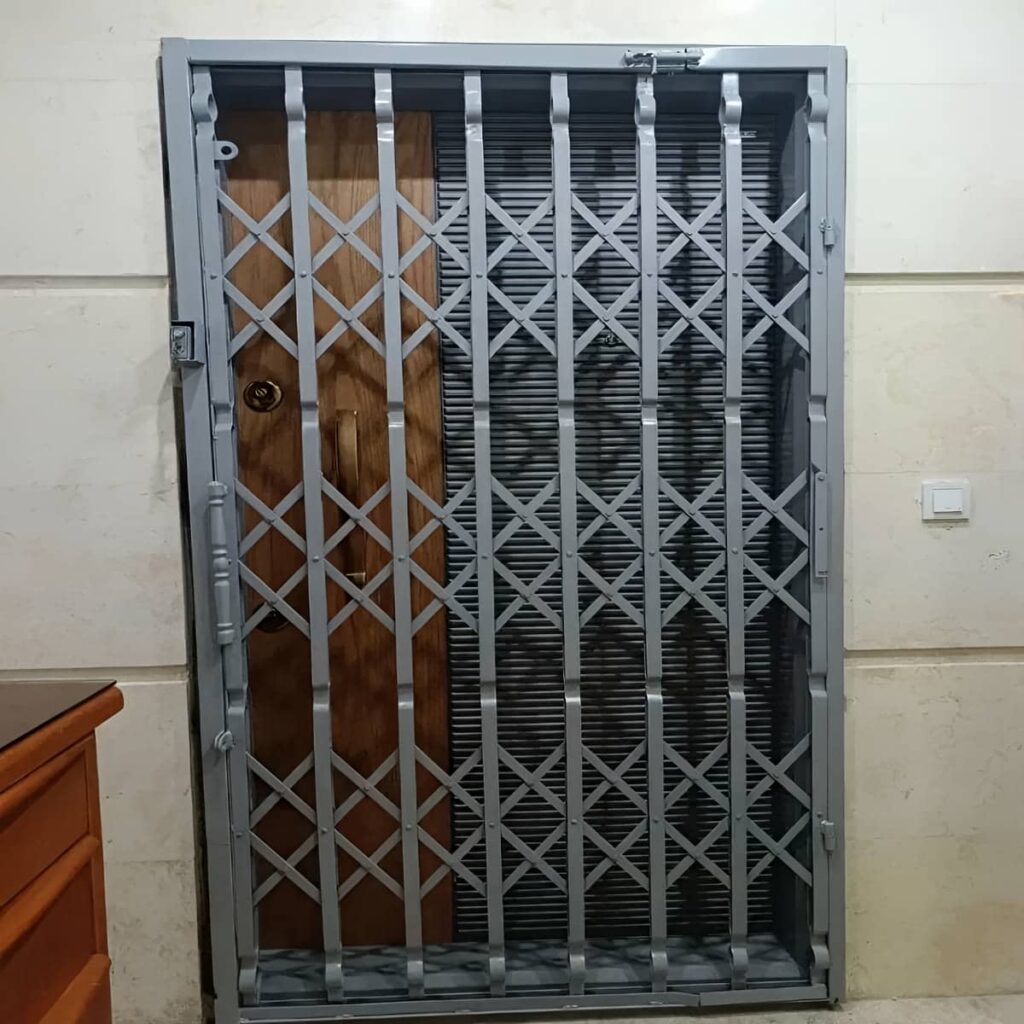 حفاظ درب آکاردئونی سفید کنار چارچوب ورودی ساختمان