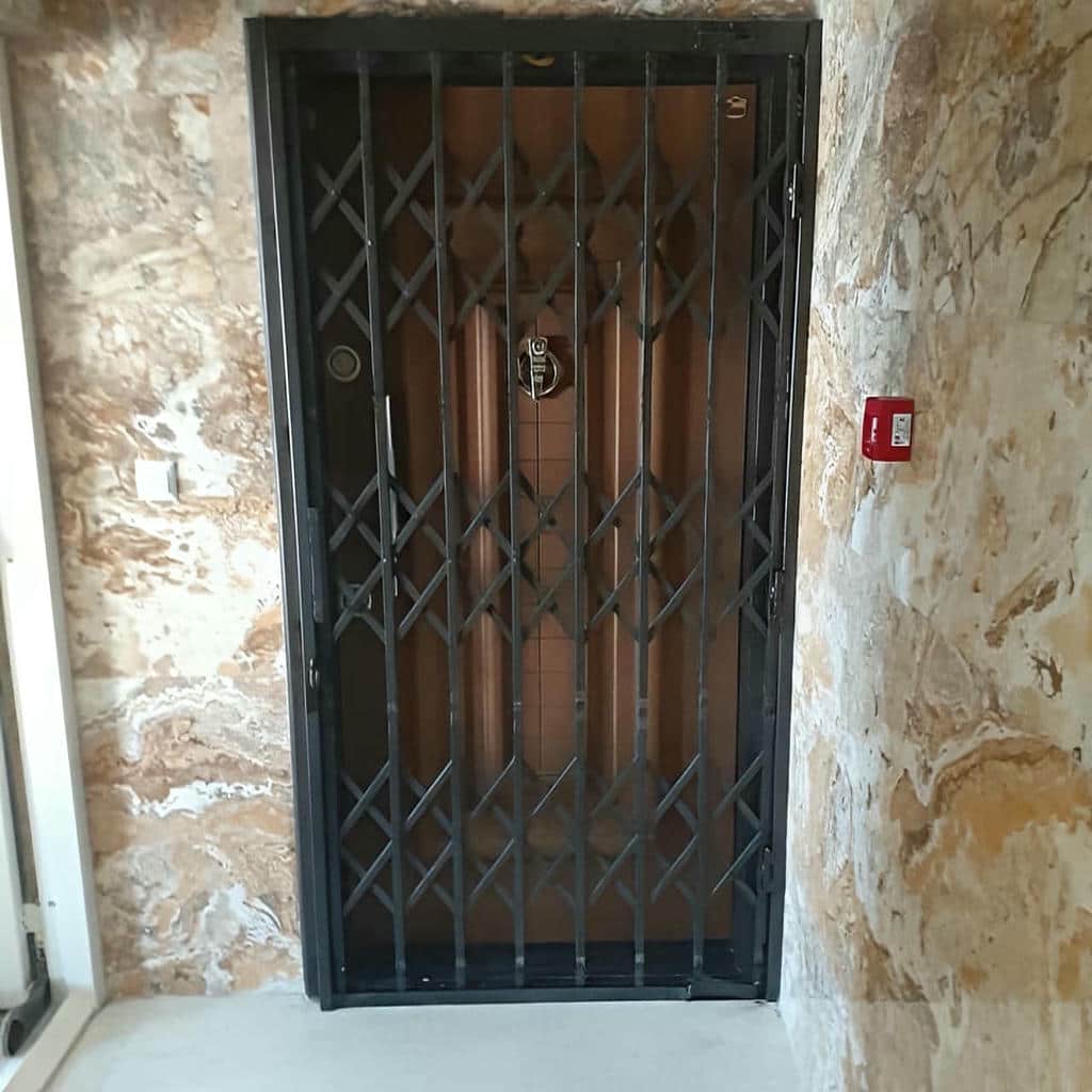 حفاظ درب آکاردئونی مشکی کنار دیوار سنگی